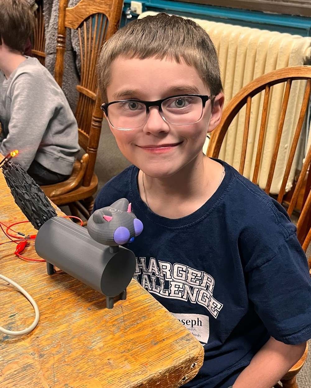 A Design Your World student at a workbench with the robotic pet he built, its wiring visible