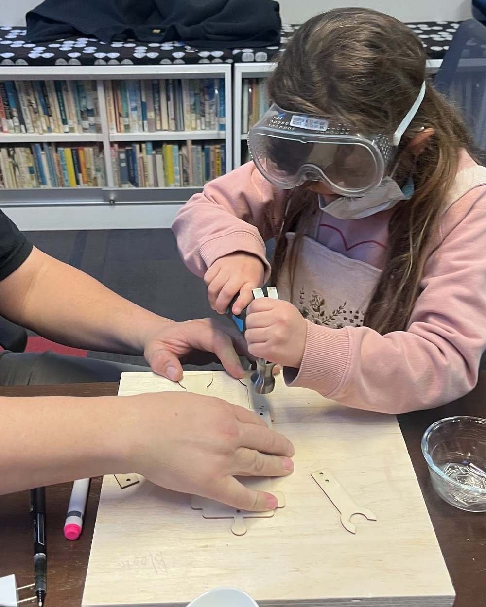 A Design Your World student in safety goggles using a power tool to shape a wooden part for her invention