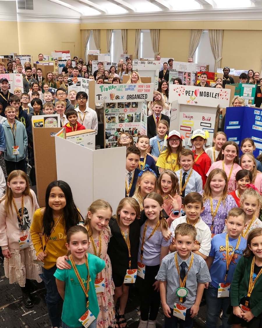 A large group of Design Your World students gathered together at a showcase event with their project boards
